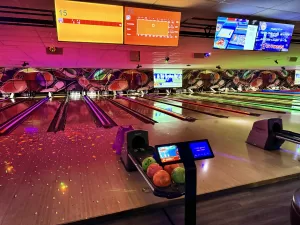 A vibrant bowling alley with neon lighting, multiple lanes, digital scoreboards, and bowling balls ready for play, creating an exciting atmosphere for bowlers.