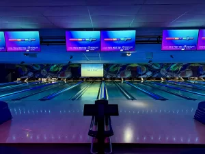 A view of bowling lanes under neon lighting, featuring digital scoreboards and a modern bowling alley atmosphere.