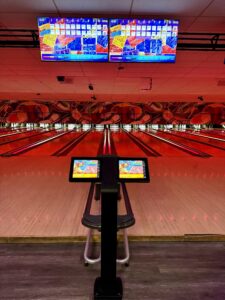 A vibrant bowling lane at Strikers Bowling in Sunrise, FL, featuring an interactive scoring system, glowing lane lights, and large digital scoreboards