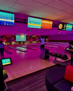 Best Bowling in Sunrise FL with neon purple lighting, digital scoreboards, and players enjoying a game at Strikers Bowling Alley.